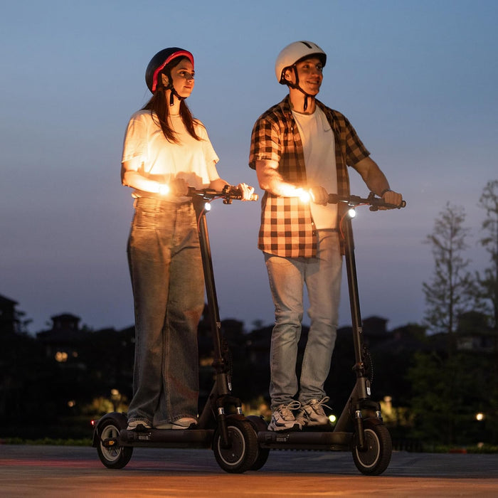 Ein Mann und eine Frau mit Helmen fahren Elektro-Scooter bei Dämmerung.